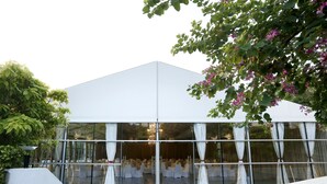 A modern building with a glass facade, white curtains, and a seating area with tables and chairs.
