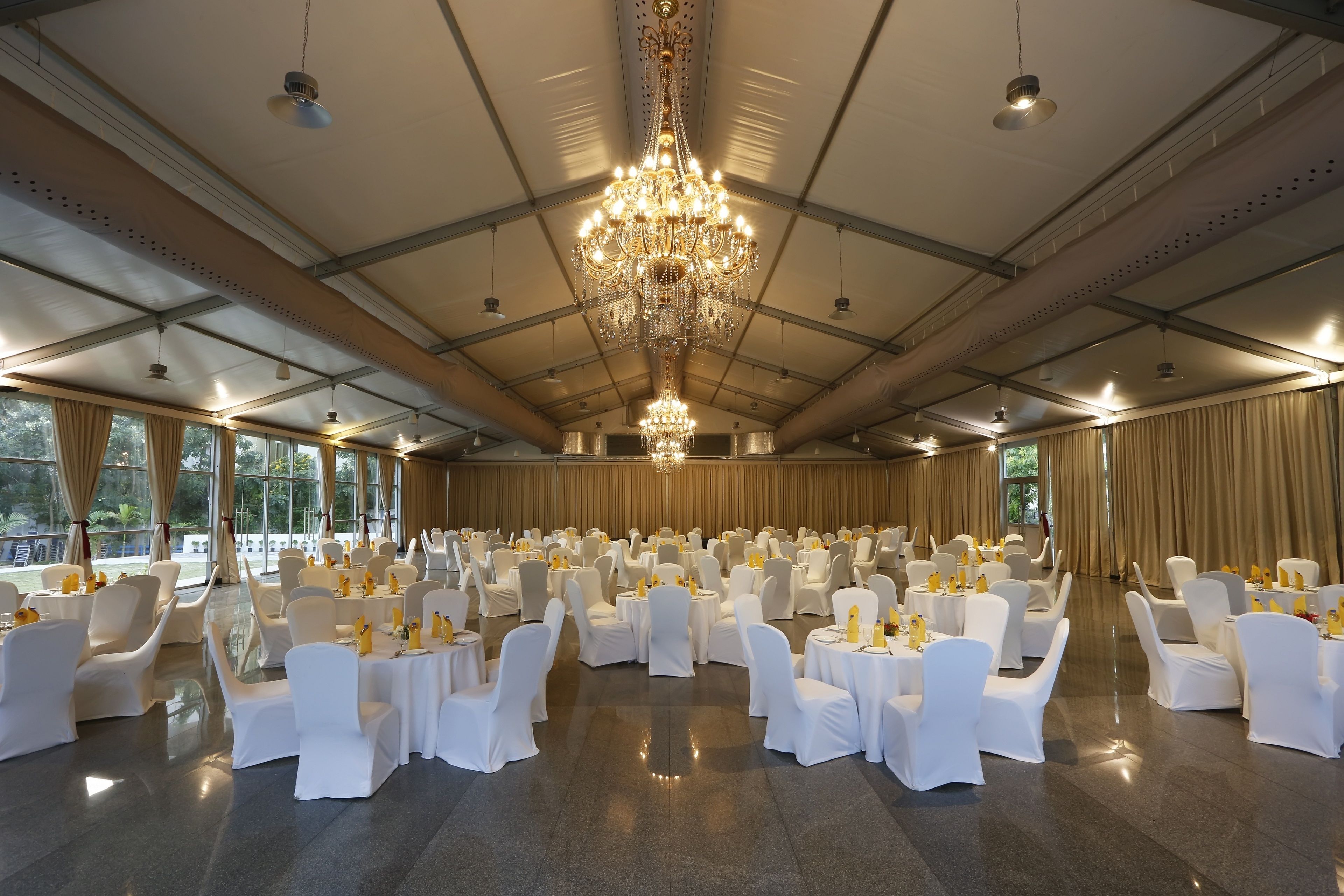 Une salle de banquet avec des tables rondes, des chaises blanches et un grand lustre.