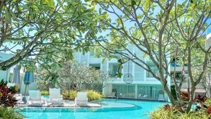 Frühstück am Pool mit Tellern voller Speisen, einem Glas Orangensaft und einer Schüssel Suppe, umgeben von üppigem Grün und blauem Himmel.
