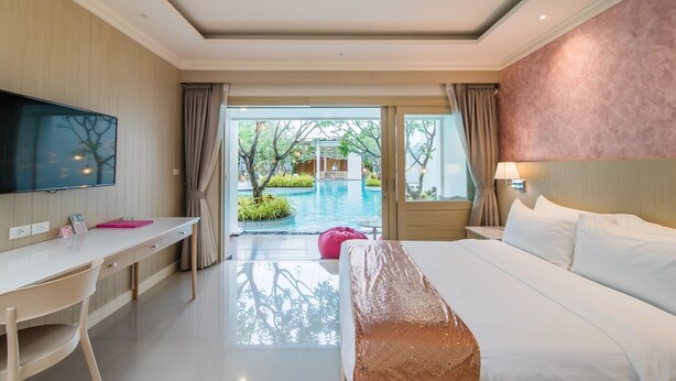 Ein Hotelzimmer mit Bett, Schreibtisch und Fernseher. Blick auf ein Außenbecken und Grünflächen.