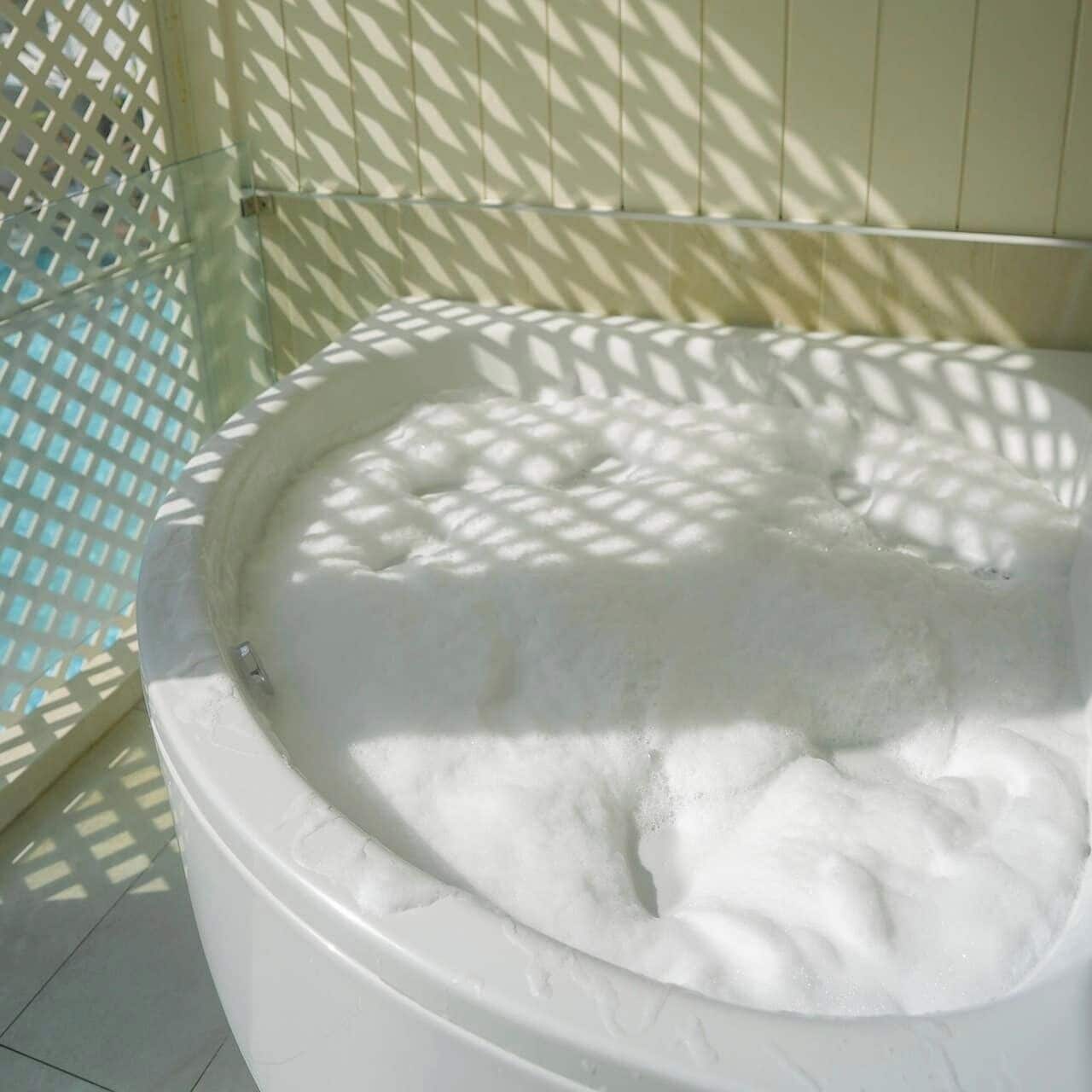 Un bain à remous rempli d’eau mousseuse, entouré d’un mur blanc et d’une structure en treillis.