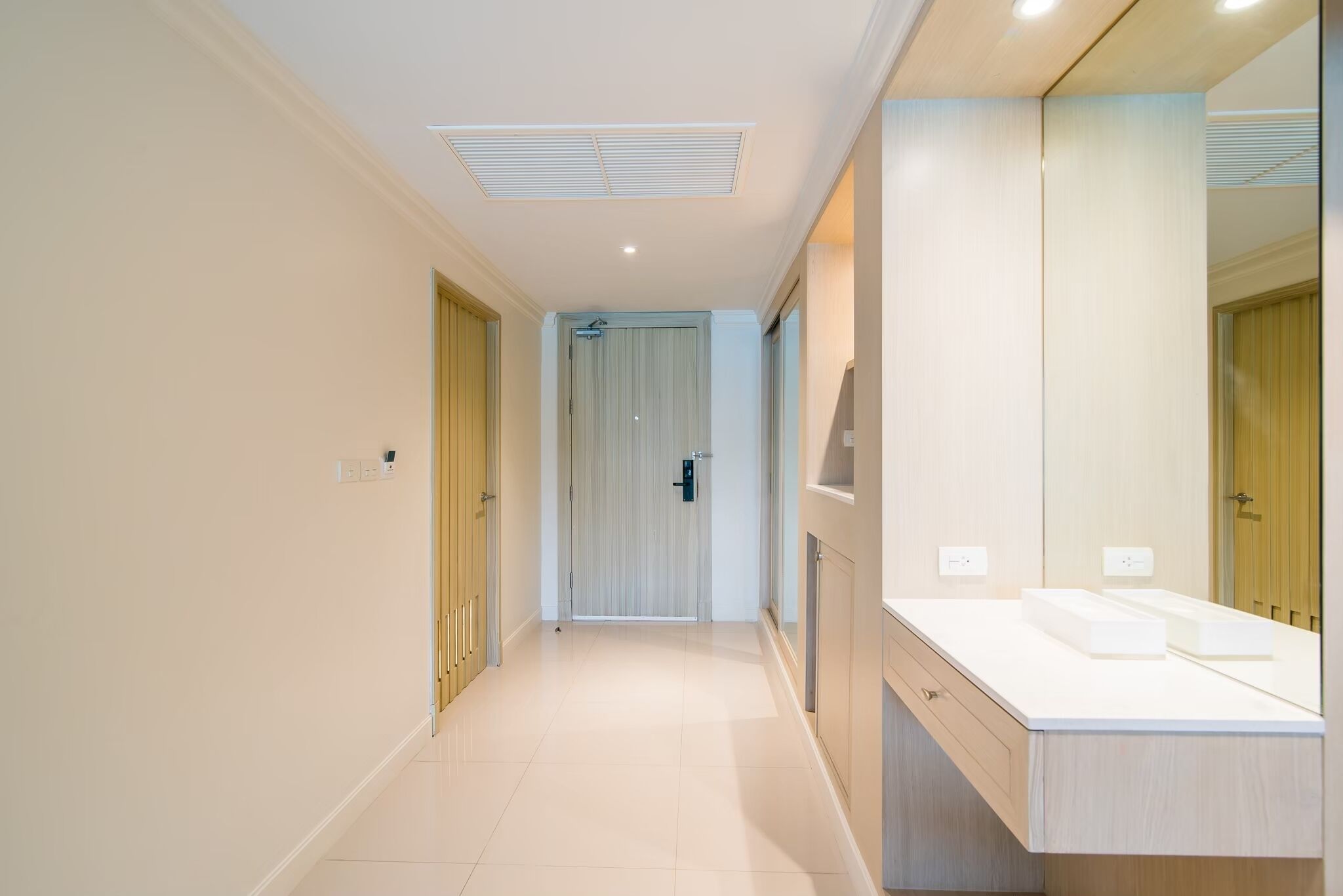 A modern bathroom with a large mirror, a white countertop, and a door leading to another room.