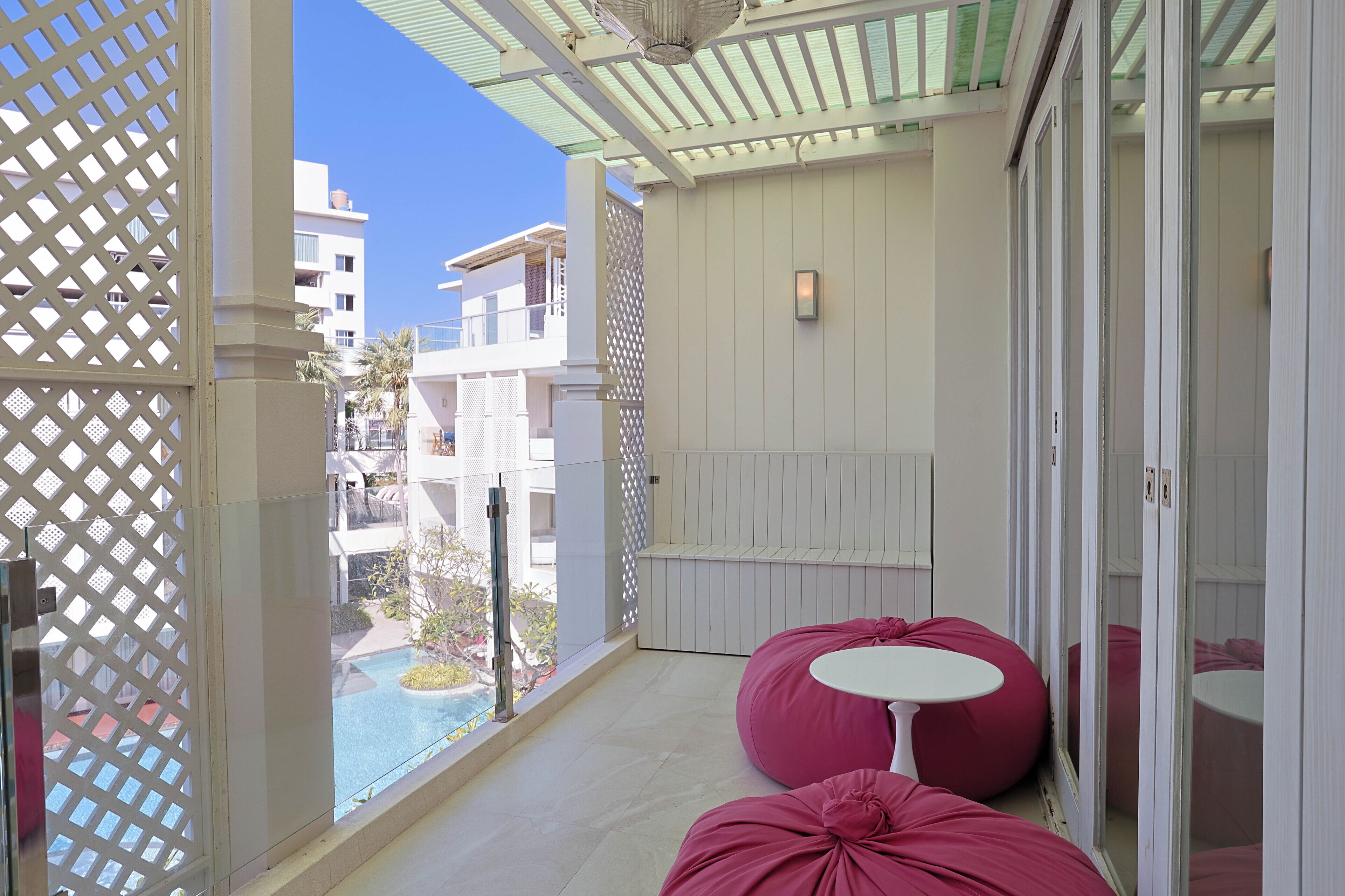 Un balcon avec vue sur la piscine, des murs blancs et deux fauteuils-pouf roses.