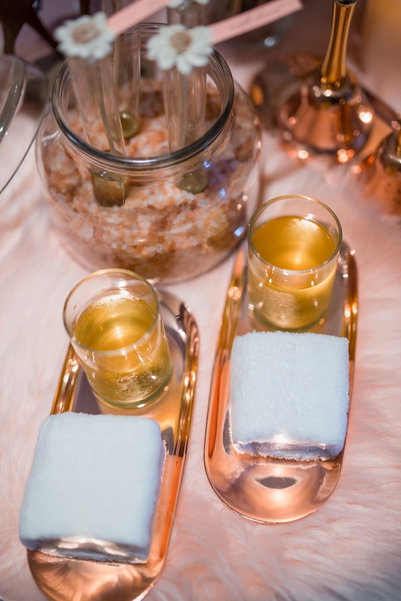Un tavolo con due bicchierini di vetro contenenti un liquido dorato, ognuno con un tovagliolo bianco.