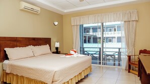 A hotel room with a large bed, a nightstand, a lamp, a balcony with a view of buildings, and an air conditioning unit. - Hotel Casona del Lago (Flores)