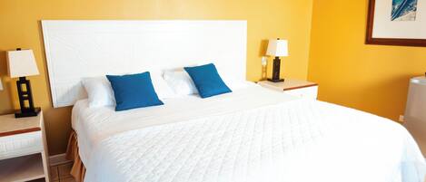 Una habitación de hotel con una cama grande, una mesita de noche, una lámpara, aire acondicionado y ventilador de techo.