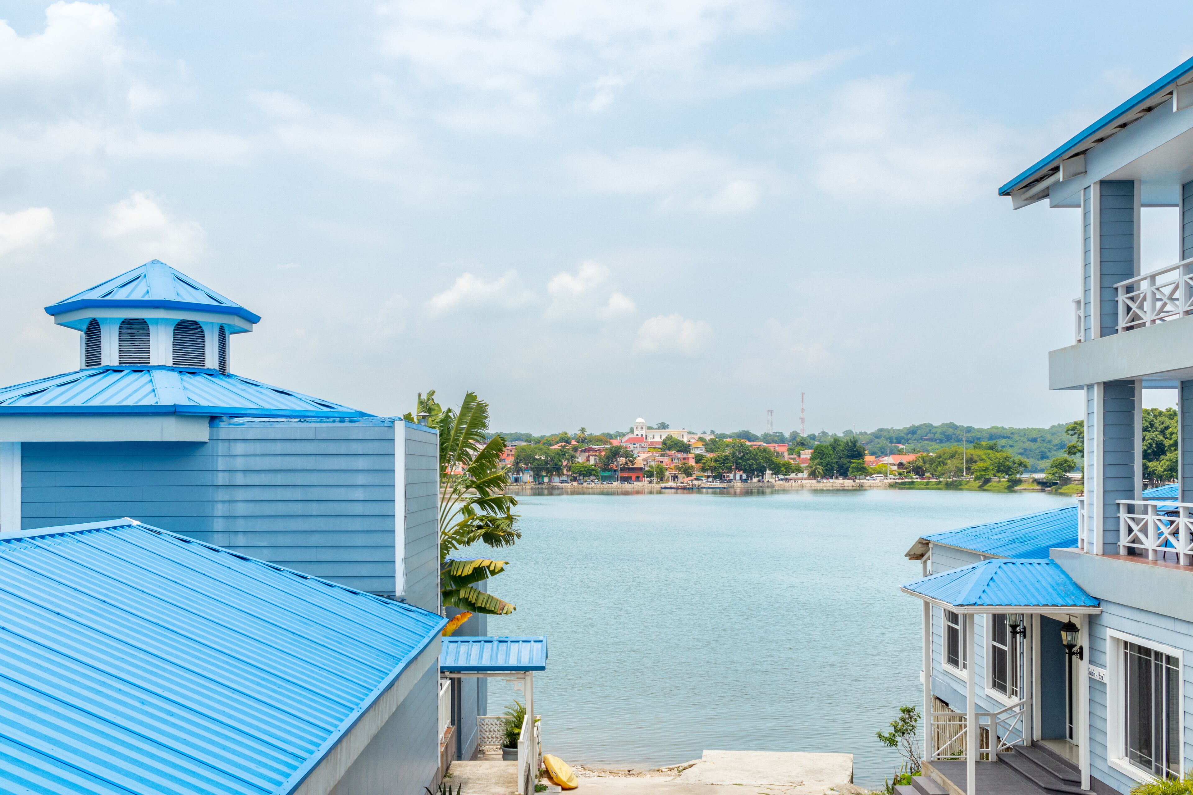A view of a waterfront property with blue-roofed buildings, a clear sky, and a distant town across the water.
