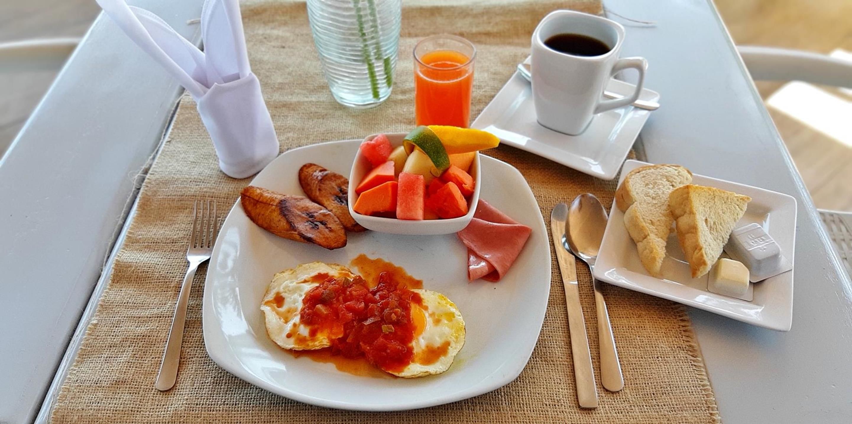 Une table mise pour le petit-déjeuner avec une assiette d'œufs, des fruits, des toasts et une tasse de café.