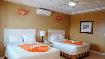 Een hotelkamer met twee bedden, een plafondventilator, een airconditioner, een ingelijst schilderij aan de muur en een telefoon op het nachtkastje.