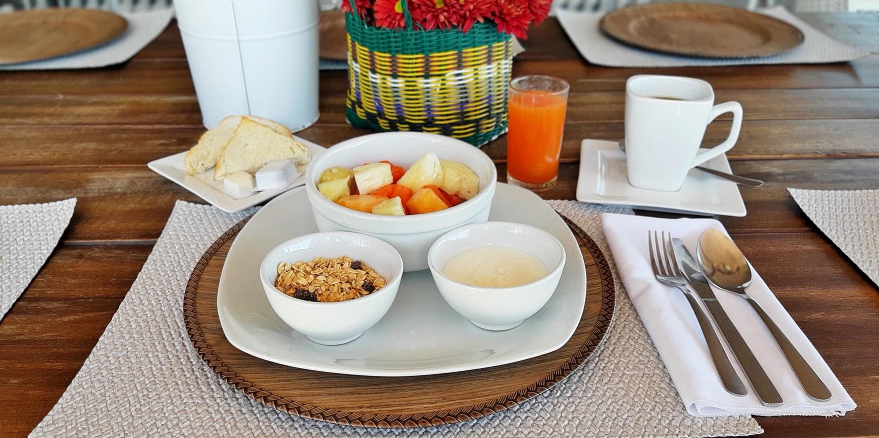 Un safata de petitdejuni amb torrades, fruita, iogurt, granola i suc d'aranja sobre una taula de fusta.