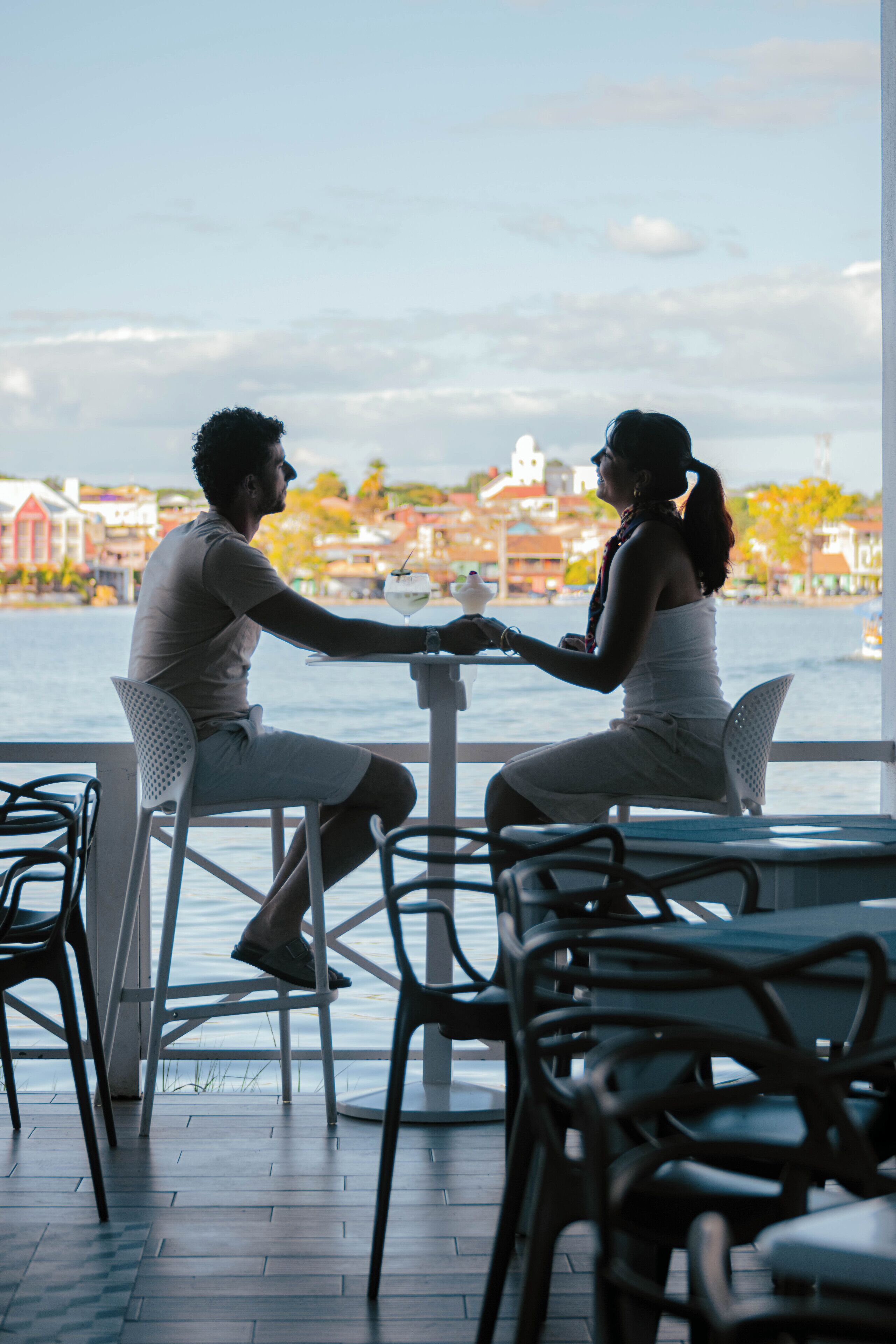 A couple dining at an outdoor table with a view of the water and buildings in the background.