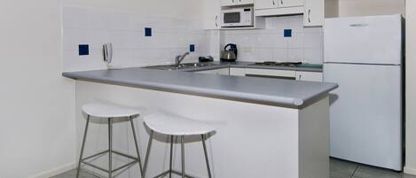 Une cuisine moderne avec des meubles blancs, un plan de travail en acier inoxydable, un four à micro-ondes, une bouilloire et deux tabourets de bar.