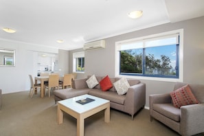 A modern living room with a sofa, armchair, and coffee table. There is a dining area with chairs and a table in the background.