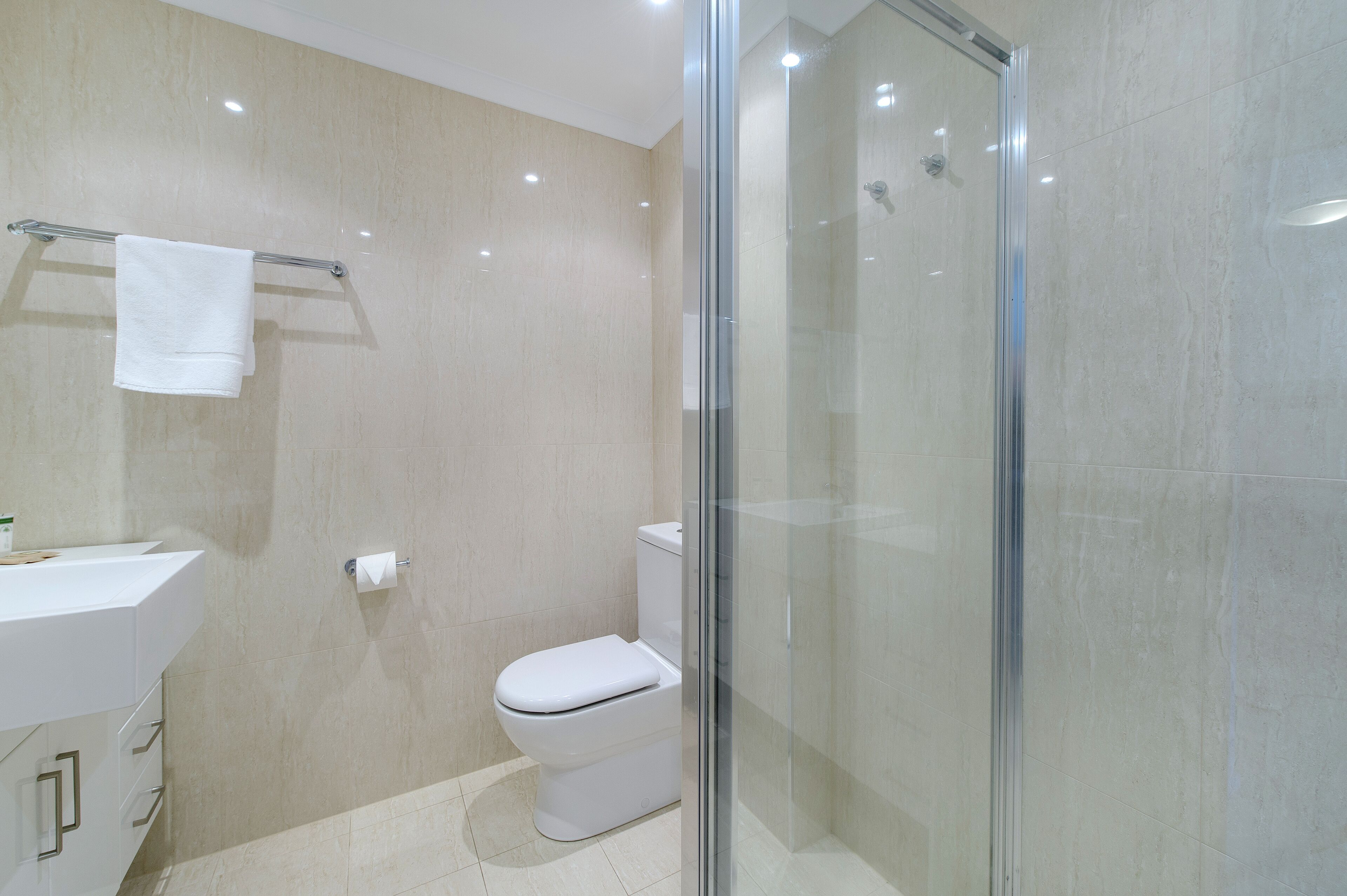 Une salle de bain moderne avec une douche à parois de verre, des toilettes blanches et un lavabo équipé d’un porte-serviettes.