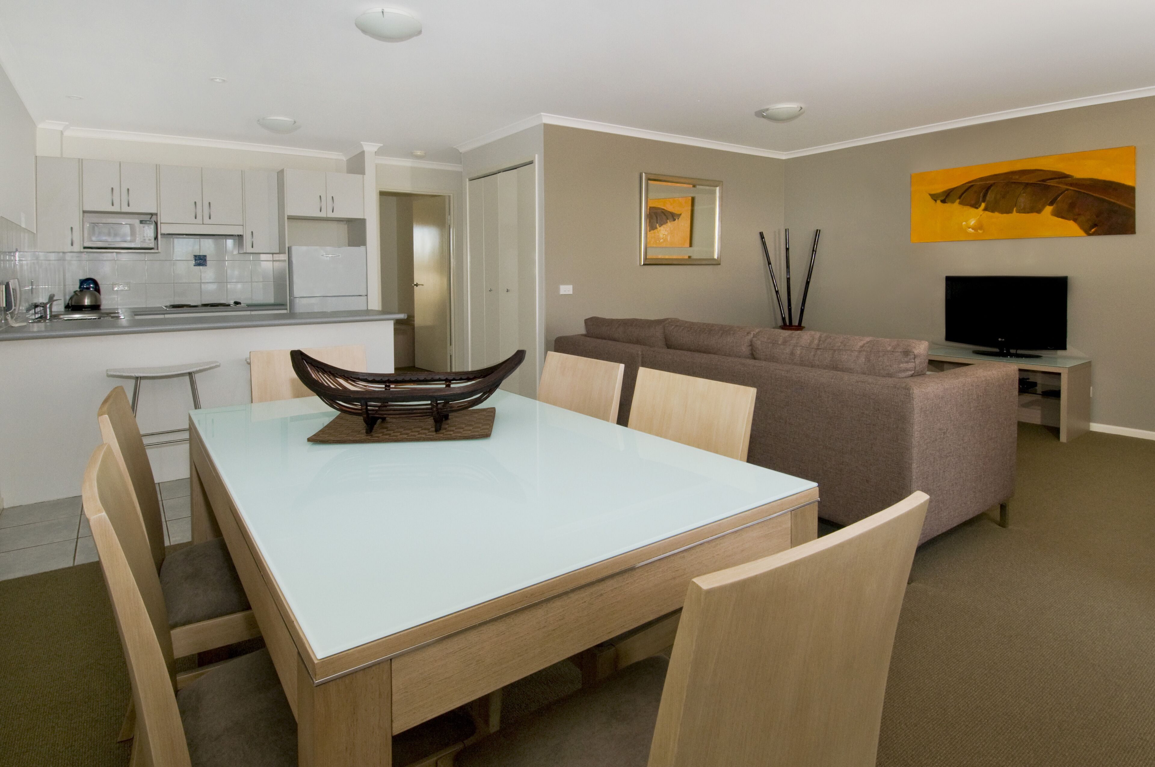 A modern living room with a dining area, a sofa, a flat-screen TV, and a kitchen in the background.