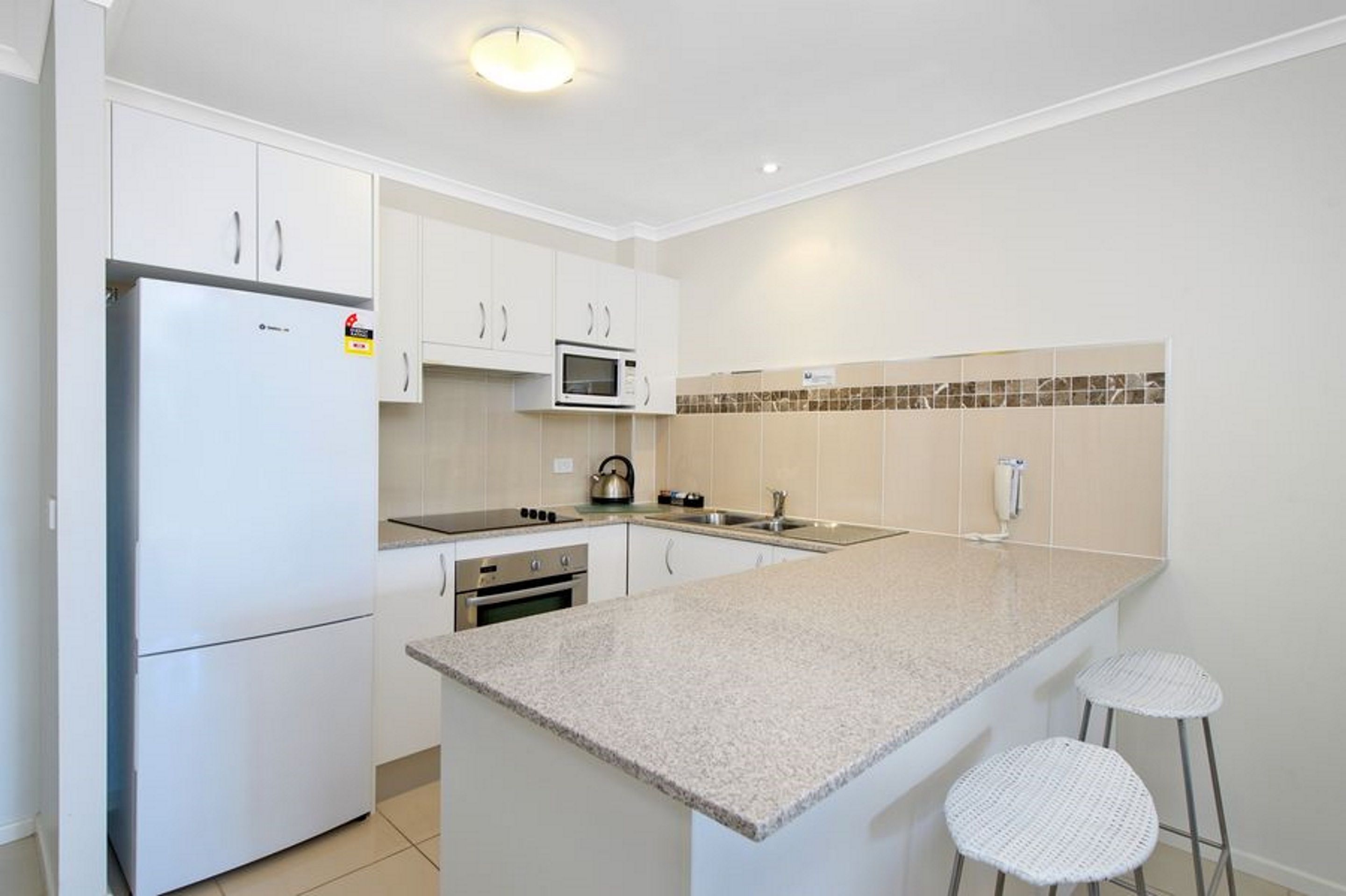 A modern kitchen with white cabinets, a built-in microwave, a kettle, and a granite countertop.
