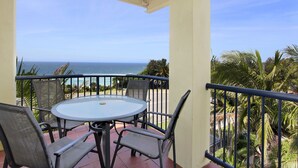 A balcony with a round table and chairs, overlooking the ocean.