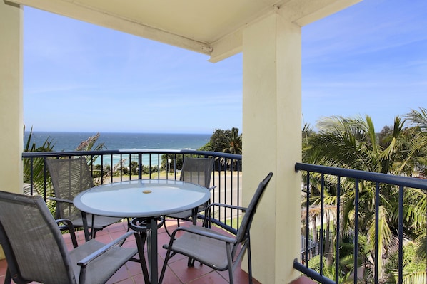 A balcony with a round table and chairs, overlooking the ocean.