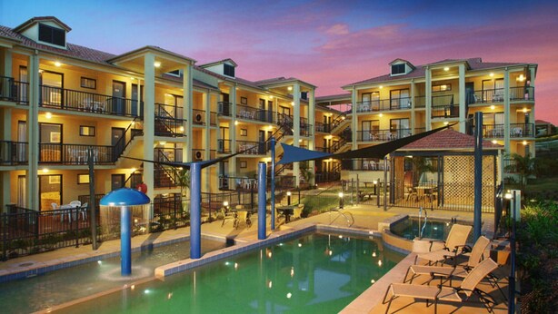A hotel with multiple balconies, a swimming pool, and outdoor seating areas.