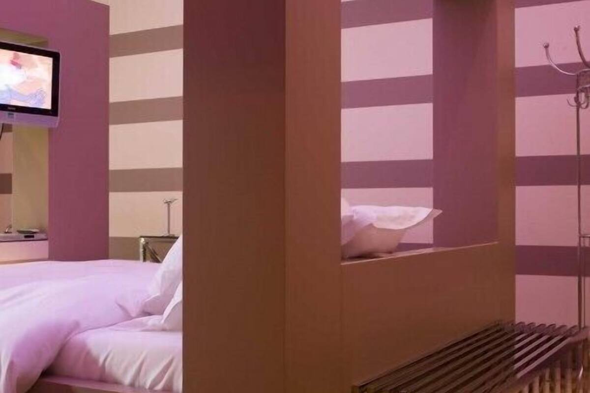 Une chambre d’hôtel avec un lit, un téléviseur fixé au mur et une fenêtre donnant sur l’extérieur.