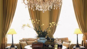 Una habitación con una gran lámpara de araña ornamentada, un sofá, una mesa redonda con adornos y dos mesitas de noche con lámparas.