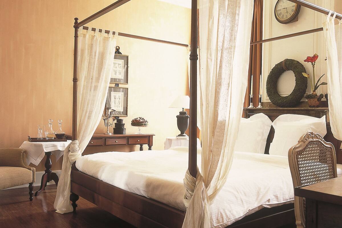 Un lit à baldaquin, une table de chevet en bois avec une lampe, une chaise et une horloge murale.