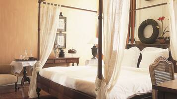 A four-poster bed with a canopy, a wooden nightstand with a lamp, a chair, and a wall clock.