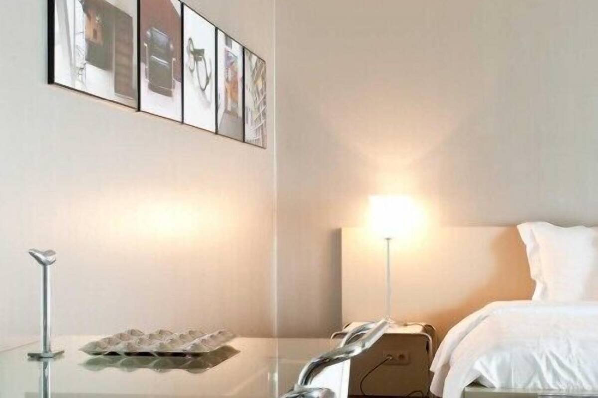 Une chambre d’hôtel avec un lit, une table de chevet avec une lampe, un cadre photo accroché au mur et une table en verre sur laquelle se trouve un plateau d’œufs.