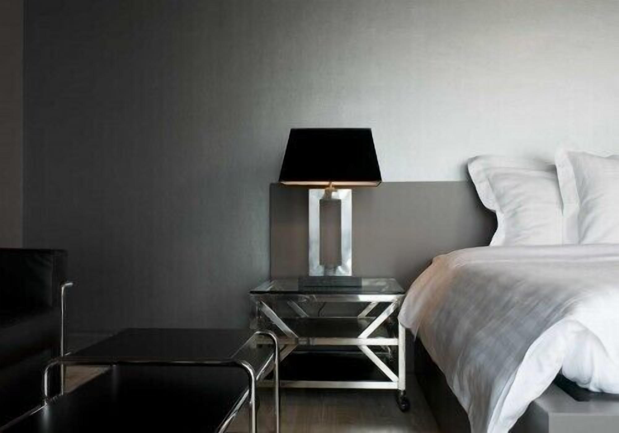 Una habitación de hotel moderna con una cama, una mesita de noche con lámpara, una pequeña mesa y una silla.