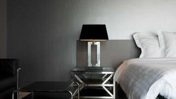 Una habitación de hotel moderna con una cama, una mesita de noche con lámpara, una pequeña mesa y una silla.
