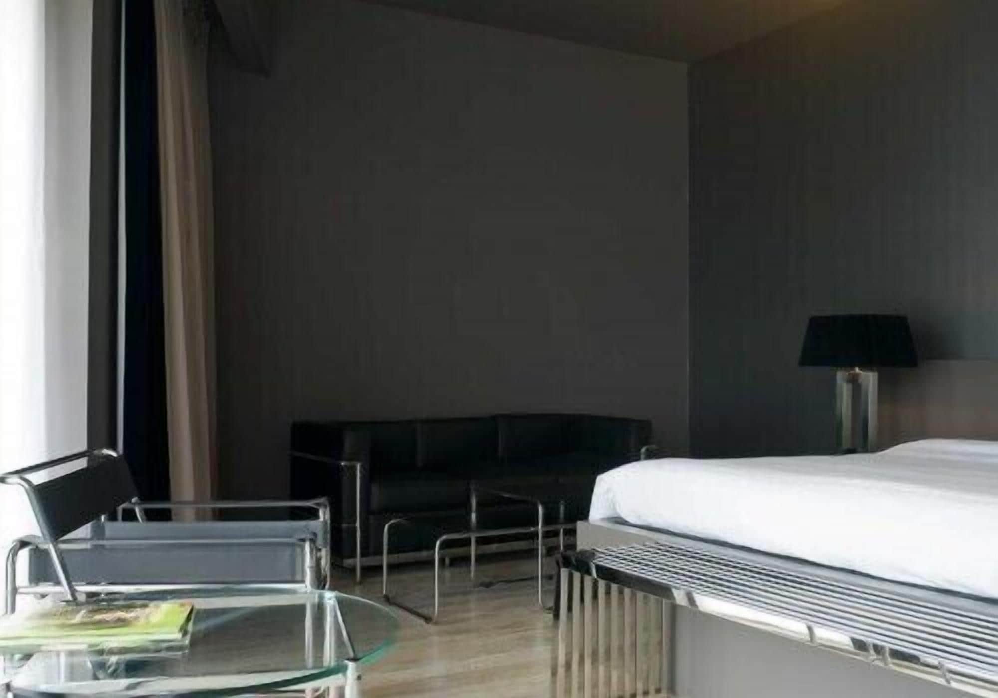 Ein Hotelzimmer mit einem Bett, einem Glastisch mit einer Zeitschrift, einem schwarzen Sofa und einer Lampe.