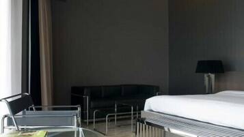 Een hotelkamer met een bed, een glazen tafeltje met een tijdschrift, een zwarte bank en een lamp.