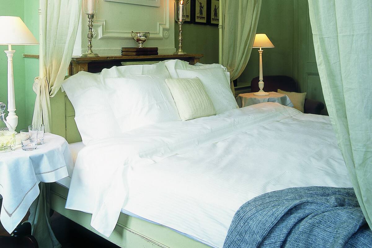 Un lit à baldaquin avec du linge de lit blanc, une table de chevet avec une lampe et un miroir au-dessus du lit.