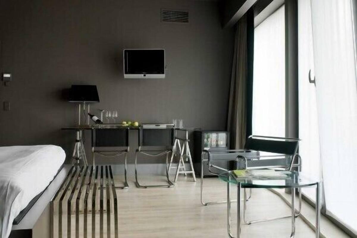 Une chambre d’hôtel avec un lit, un bureau et une chaise, une télévision et une grande fenêtre.