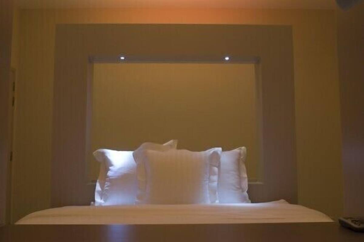 Une chambre d’hôtel avec un lit, des oreillers et une télécommande sur la table de chevet.