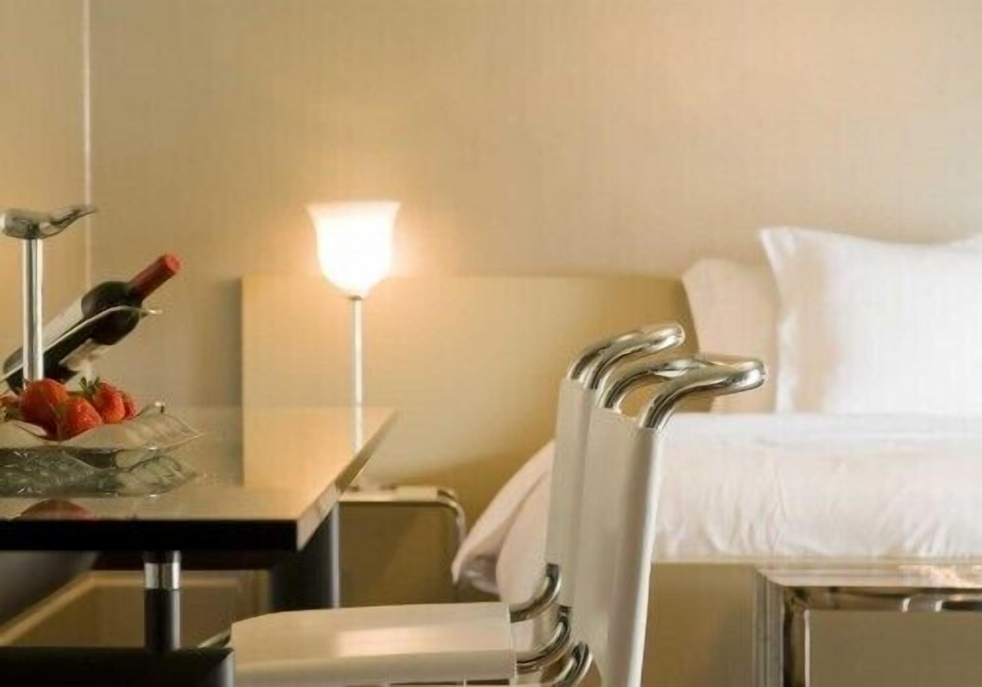 A hotel room with a bed, a desk with a lamp, and a chair.