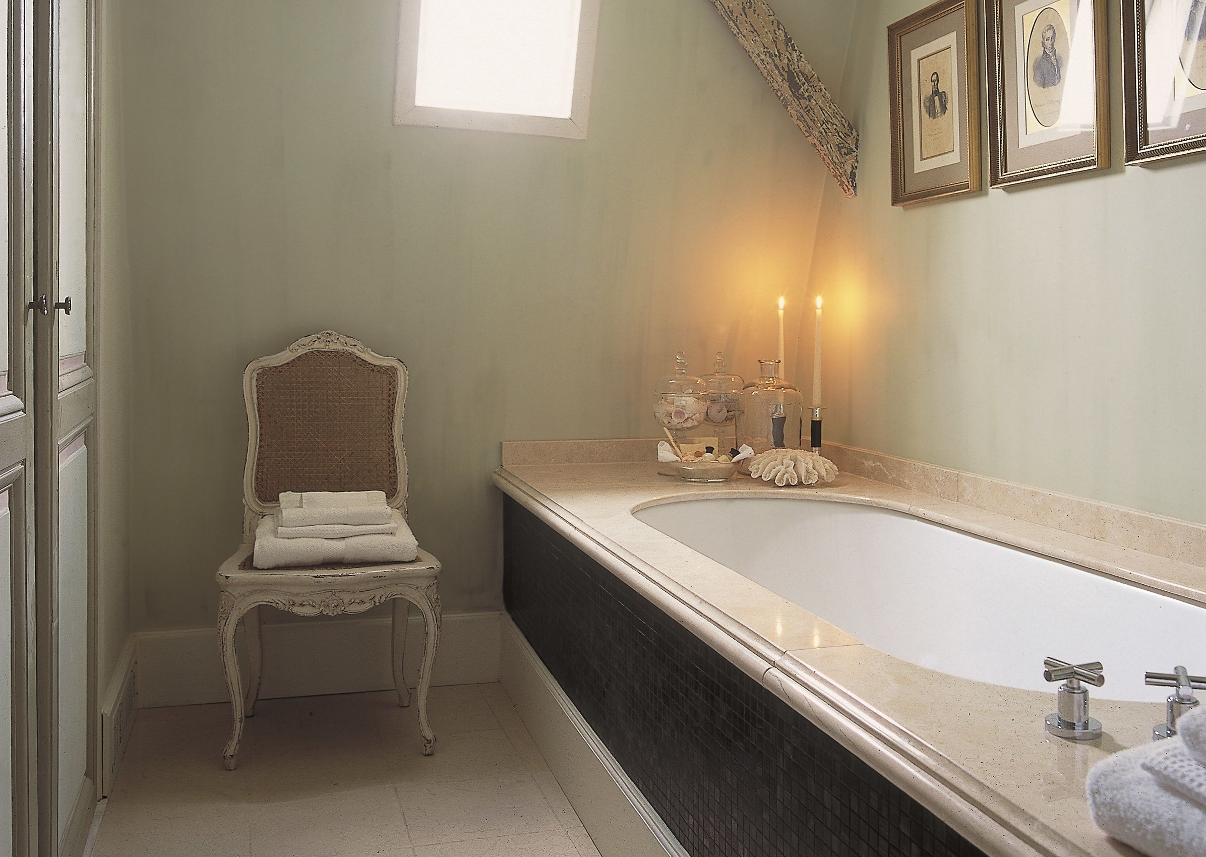 Un baño con una bañera grande, una silla decorativa y cuadros en la pared.