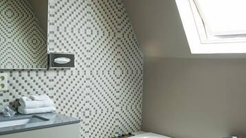 A modern bathroom with a geometric patterned wall, a built-in sink, a mirror, and a window above the bathtub.