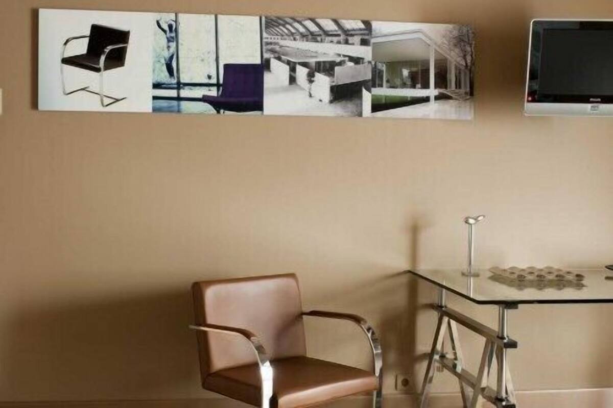 Une pièce avec une table en verre, un fauteuil en cuir marron et une série de tableaux encadrés accrochés au mur.