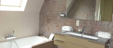 Un baño moderno con una bañera independiente, un espejo grande y un tocador con lavabo y perchero para toallas.