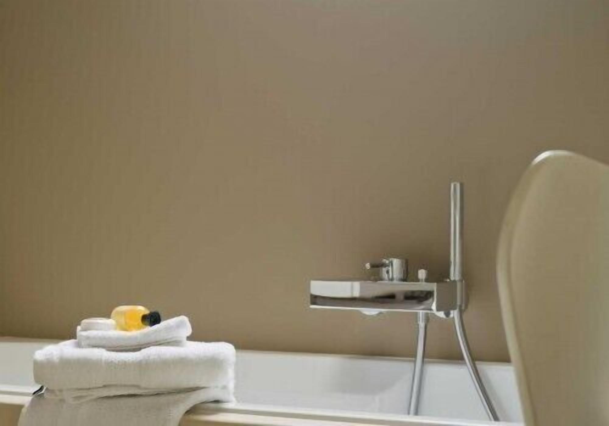 Une salle de bain avec une baignoire blanche, un robinet chromé et une serviette accompagnée de produits de toilette.