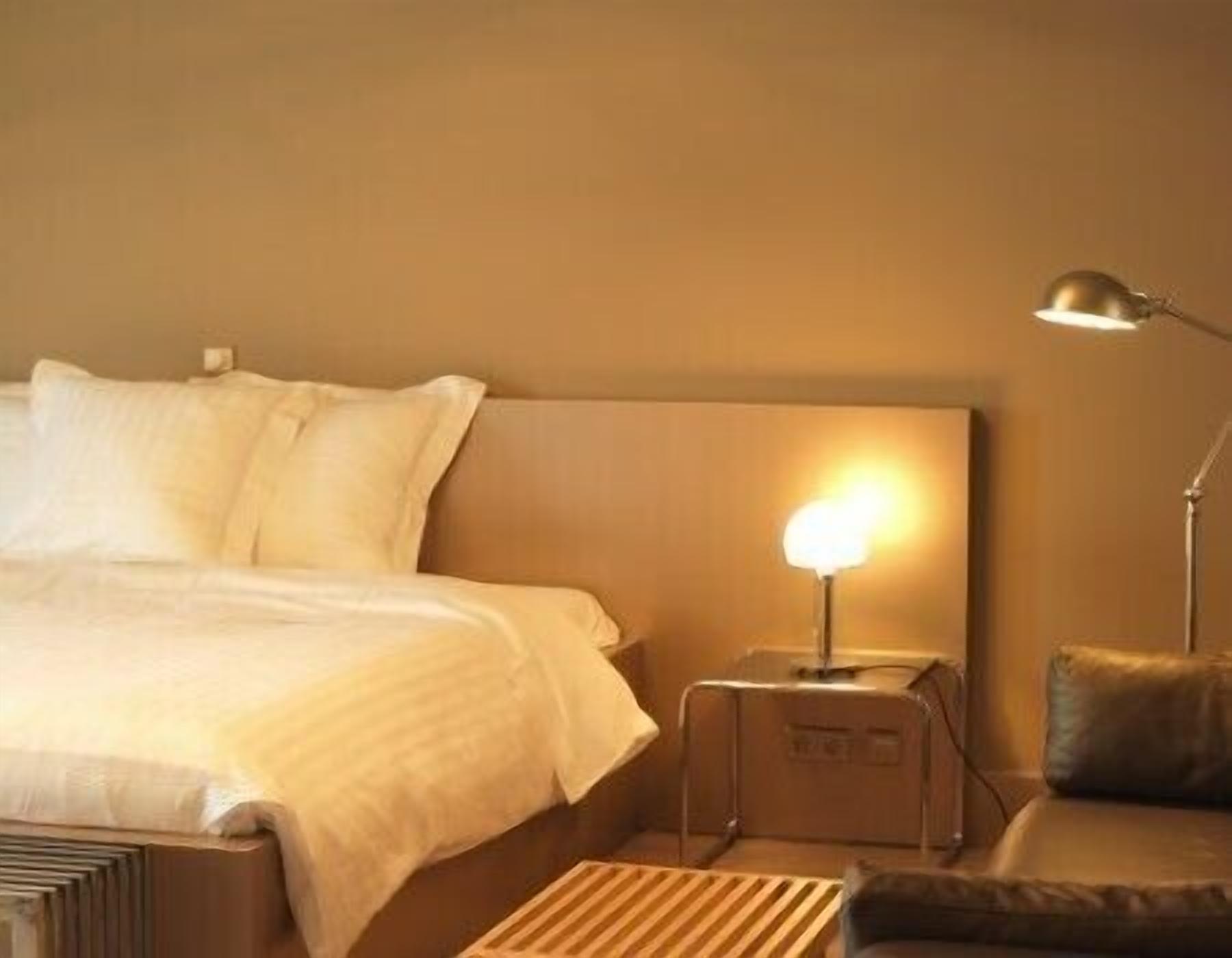 Een hotelkamer met een bed, nachtkastje, lamp en een klein zithoekje.