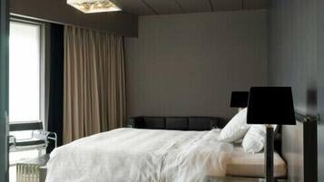 A modern hotel room with a bed, a desk, and a lamp.