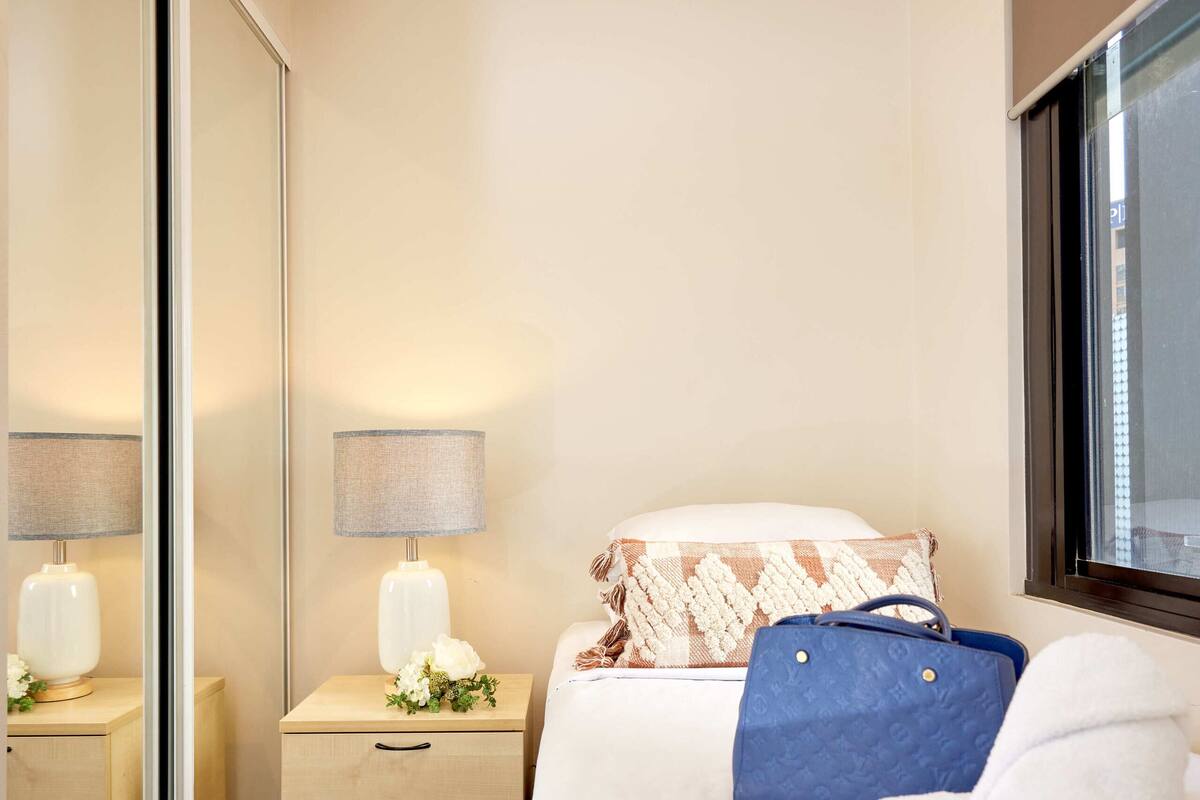 Habitación de hotel con cama, mesita de noche con lámpara, ventana y puerta corredera.