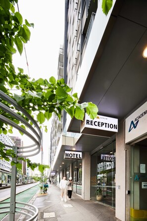 Una recepción de hotel con diseño moderno, fachada de vidrio y un cartel que indica la zona de recepción.