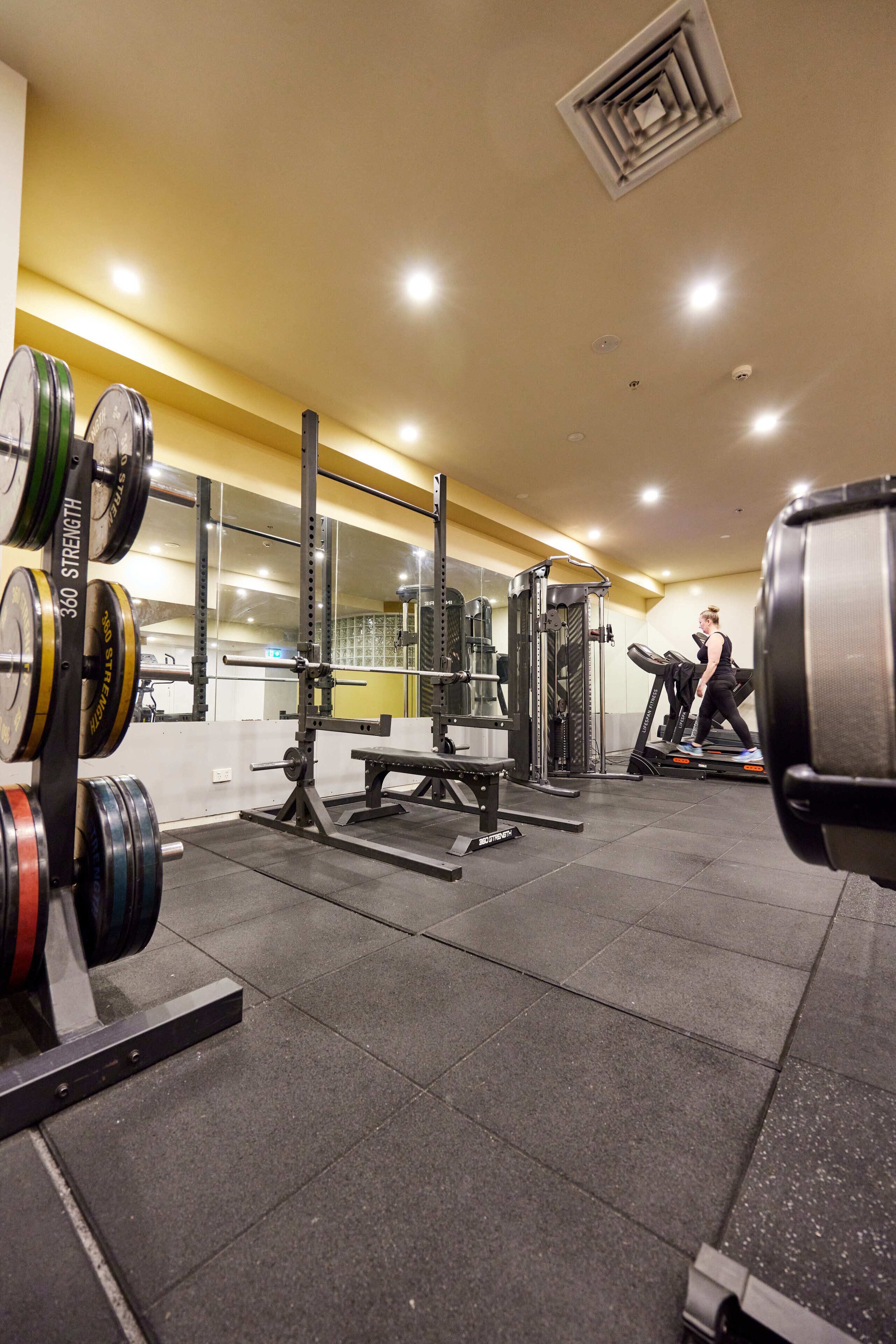 A gym with weightlifting equipment, treadmills, and mirrors on the walls.
