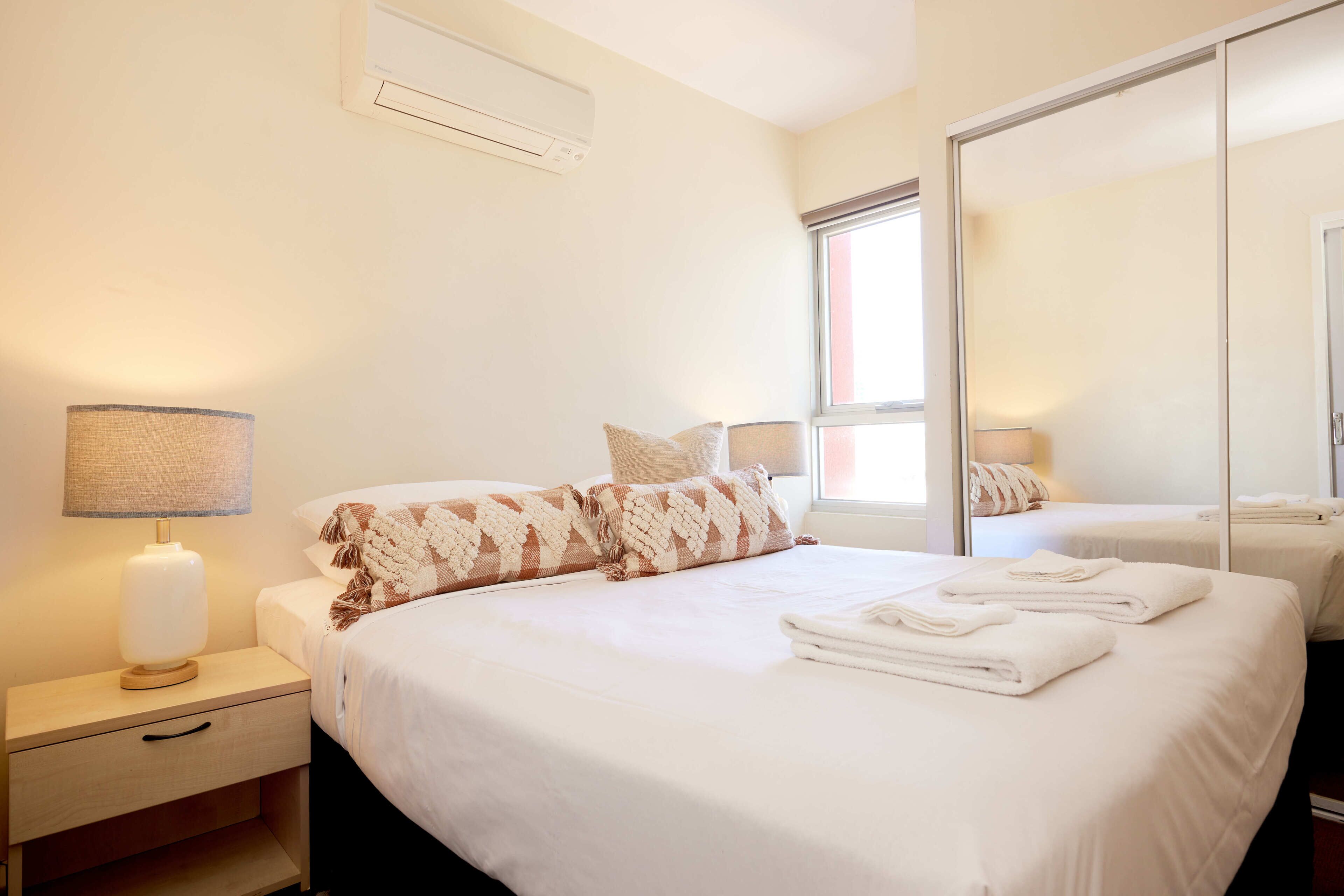 A hotel room with a bed, a nightstand, a lamp, a mirror, and a window.