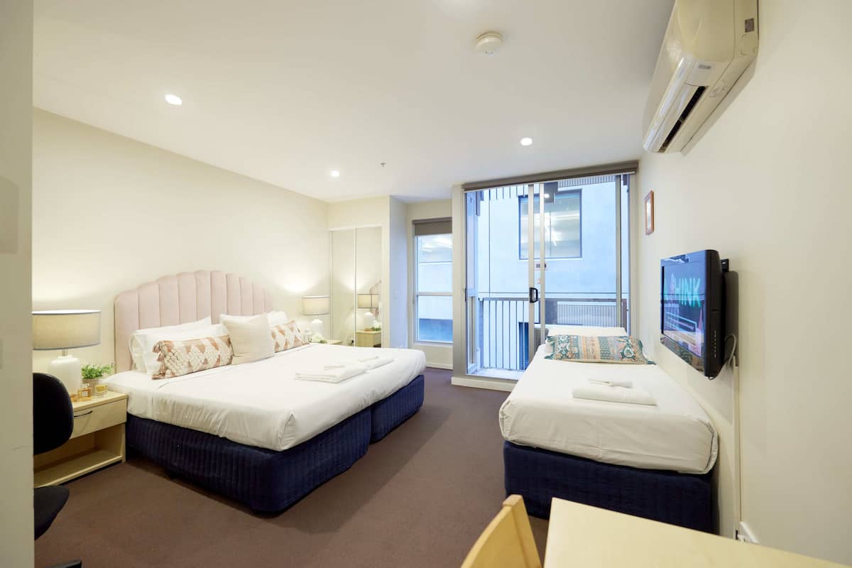 Habitación de hotel con dos camas, televisión y balcón con vistas.