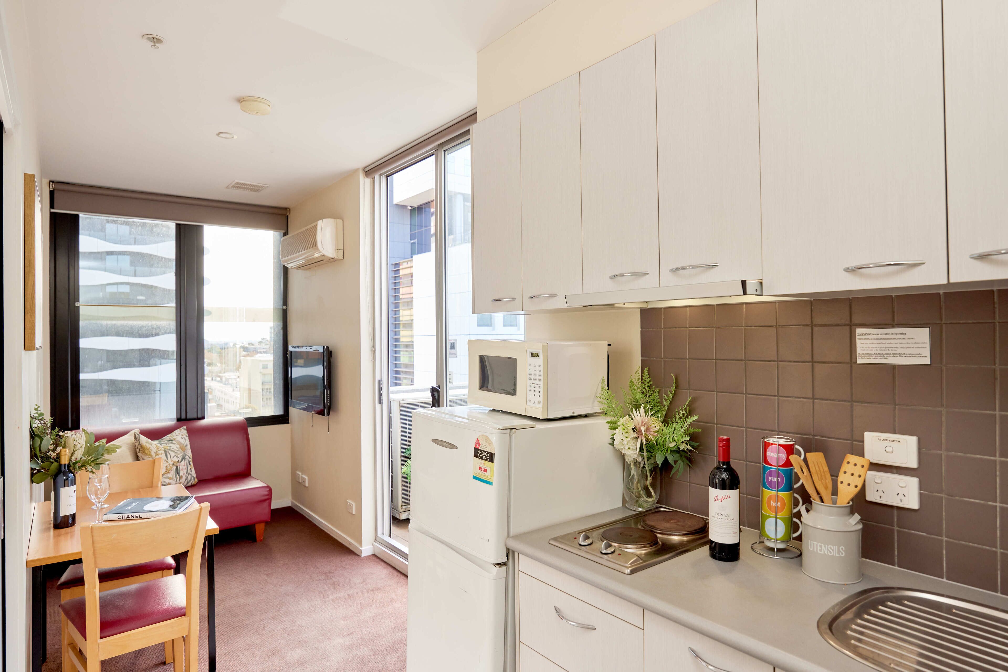 A modern kitchen with white cabinets, a microwave, a refrigerator, and a dining area with a red sofa and wooden chairs.