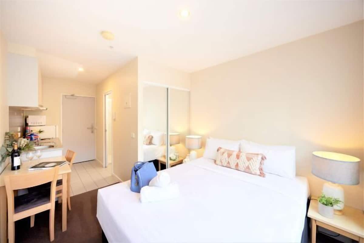 Una habitación de hotel con cama, mesita de noche, lámpara y escritorio con silla.